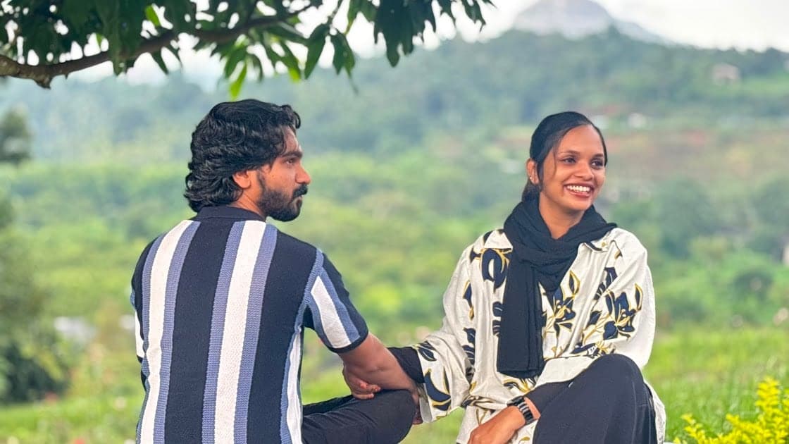Nisham and Fazna sitting on a green hillside with hills behind them, laughing
