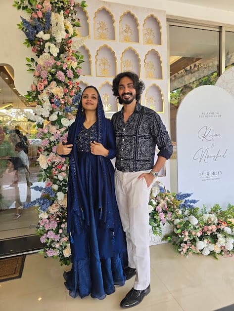 Fazna and Nisham standing in front of a wall of flowers